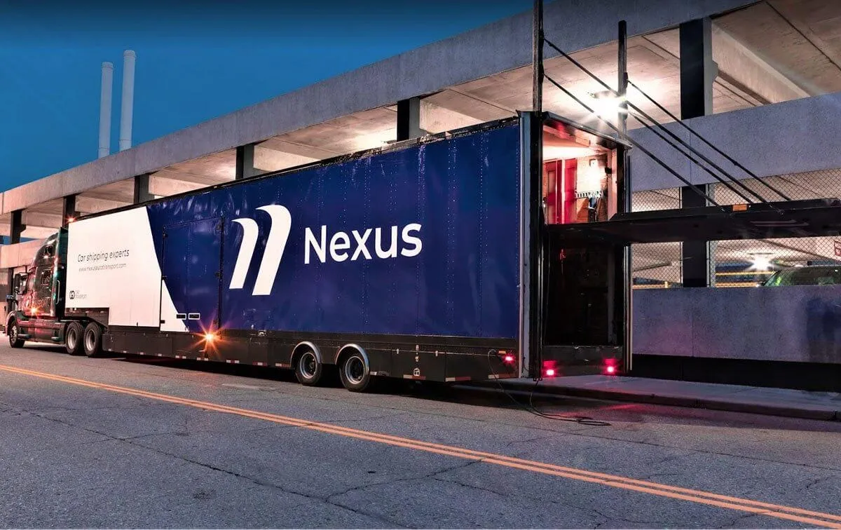 Nexus Auto Transport truck parked by a concrete building at dusk, showcasing car shipping services.
